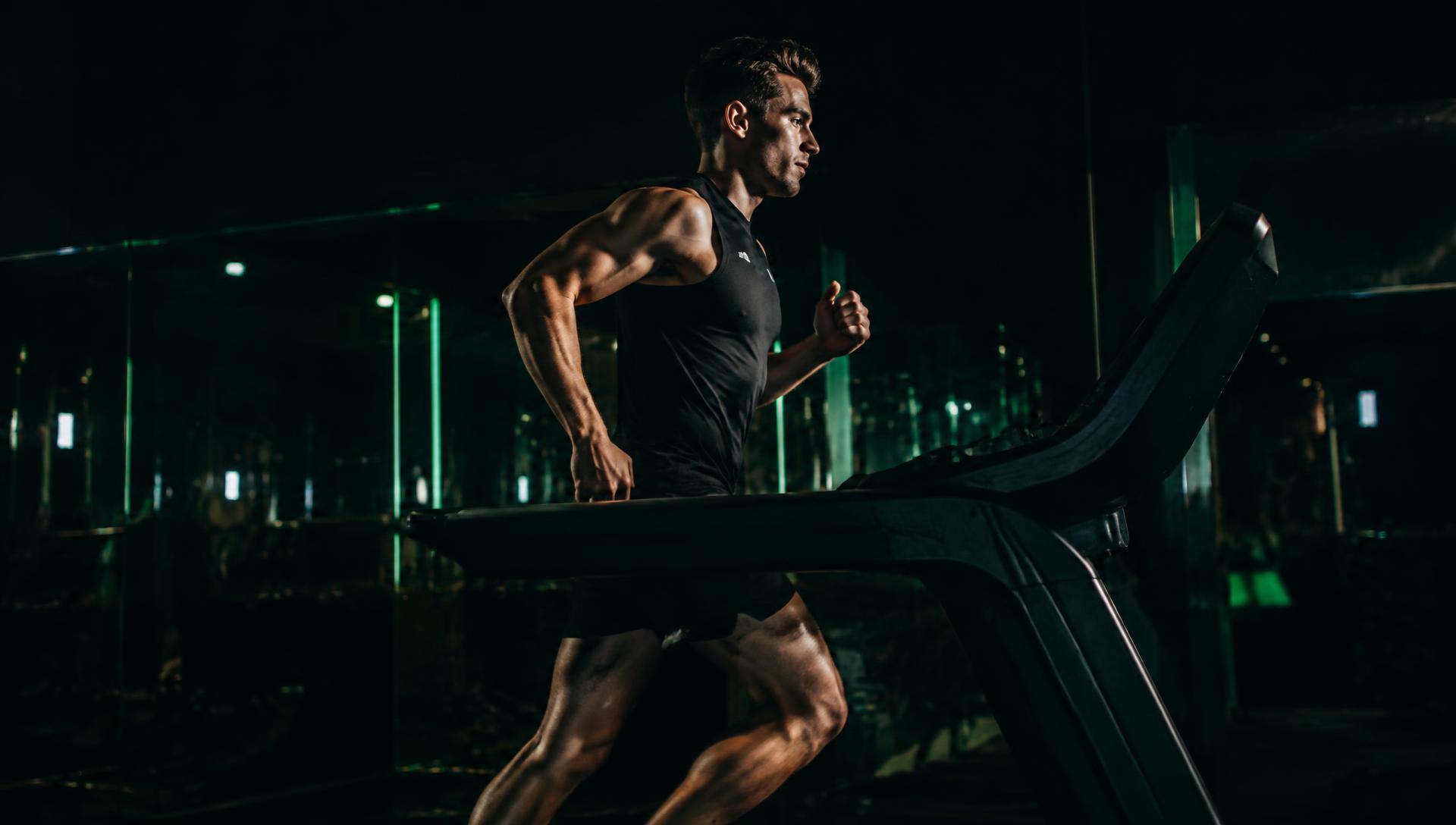 Hombre corriendo en caminadora en un gimnasio oscuro