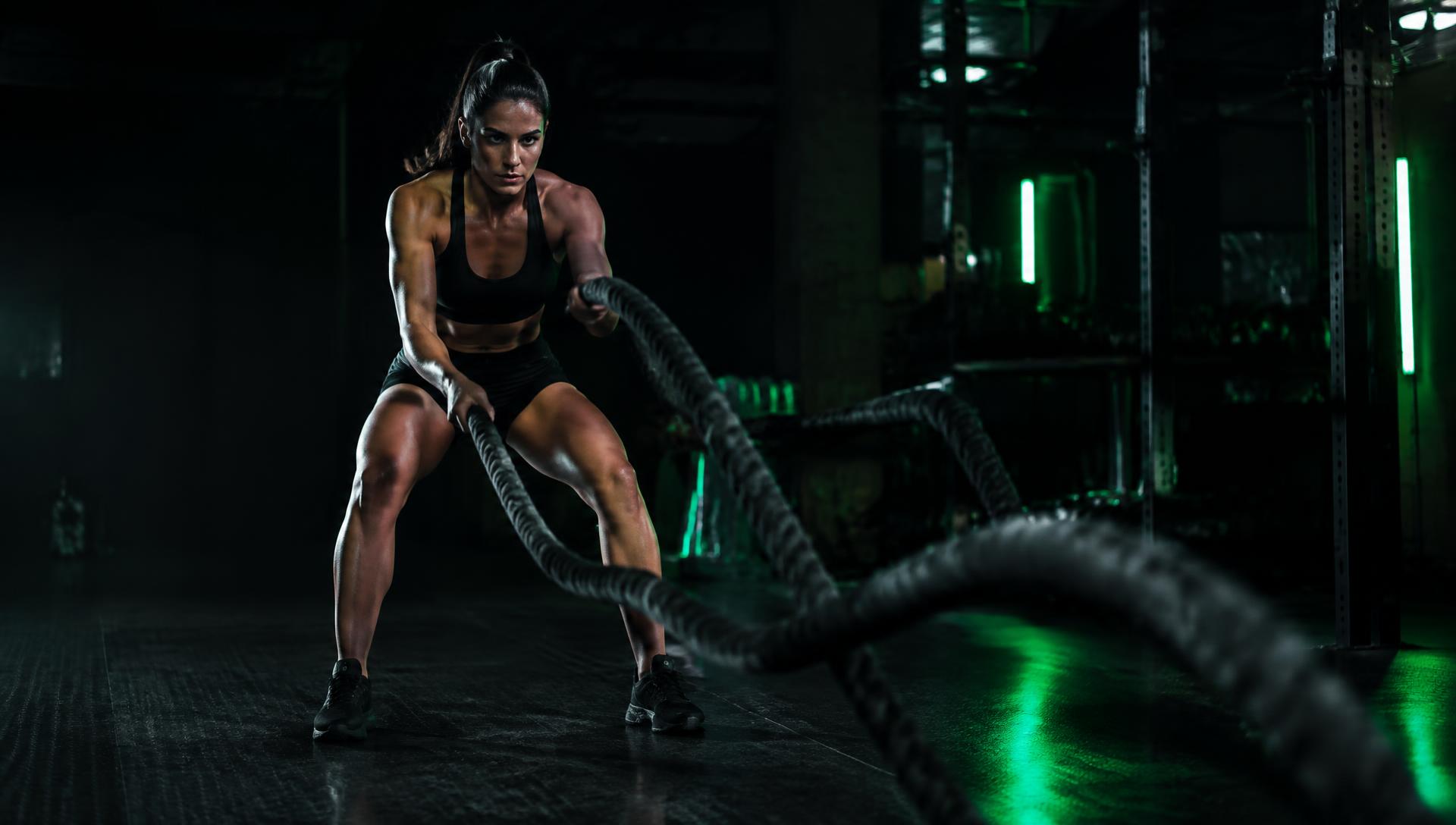 Mujer entrenando con cuerdas de batalla bajo luz verde